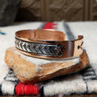 Copper and silver cuff by Robert Little featuring a repeating hand-stamped chevron or feather-inspired pattern with dark oxidized accents and polished copper borders; side view.