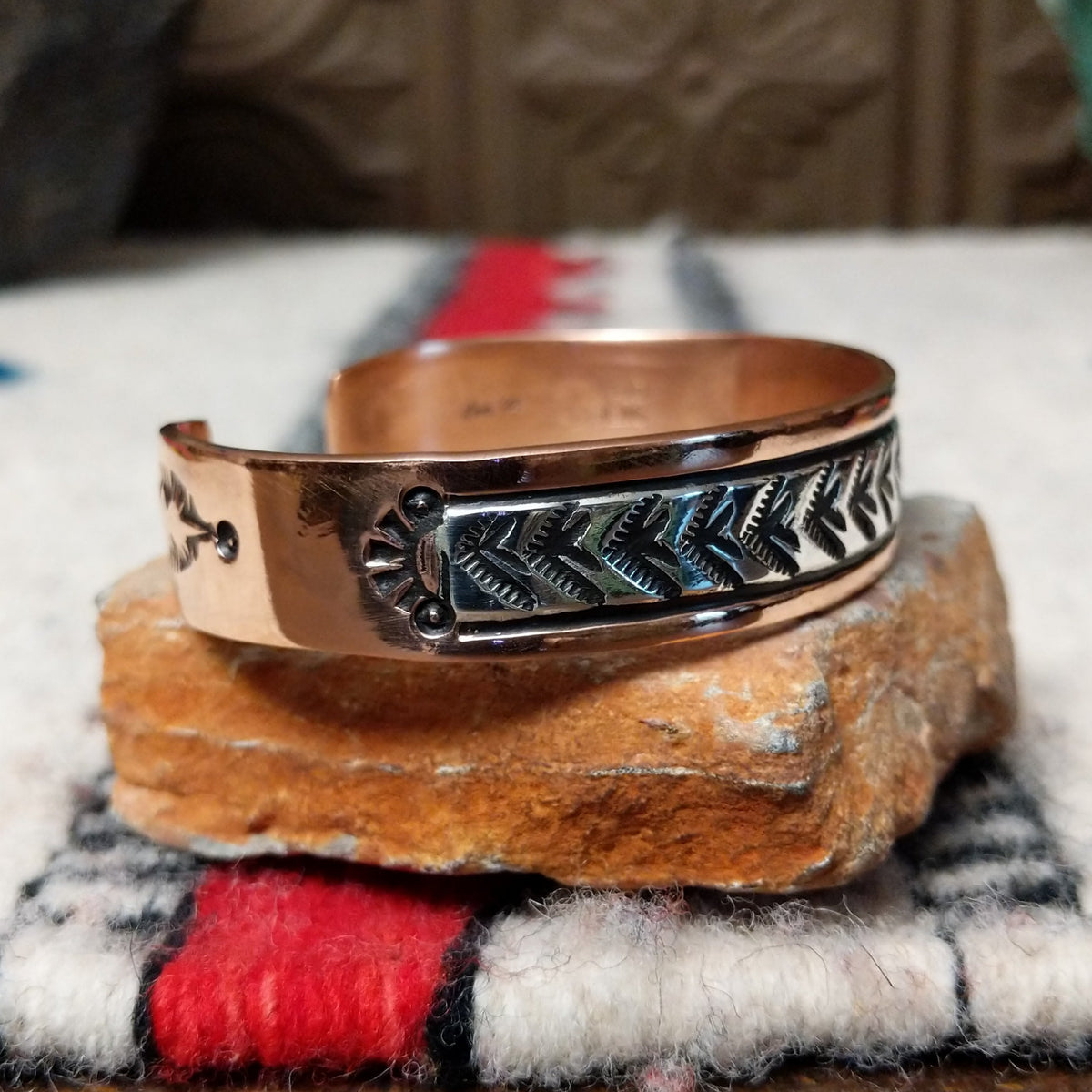 Copper and silver cuff by Robert Little featuring a repeating hand-stamped chevron or feather-inspired pattern with dark oxidized accents and polished copper borders; side view.