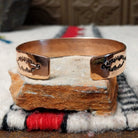 Copper and silver cuff by Robert Little featuring a repeating hand-stamped chevron or feather-inspired pattern with dark oxidized accents and polished copper borders; underside view.
