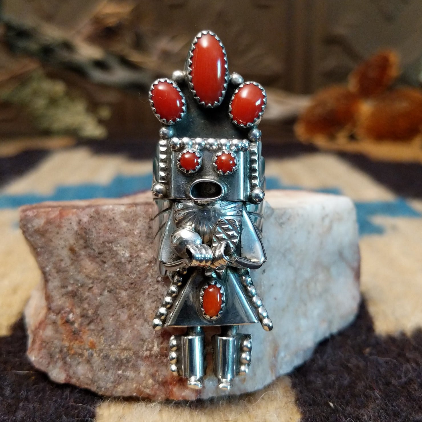 Sterling silver ring with kachina motif and coral set in bezels along the piece.