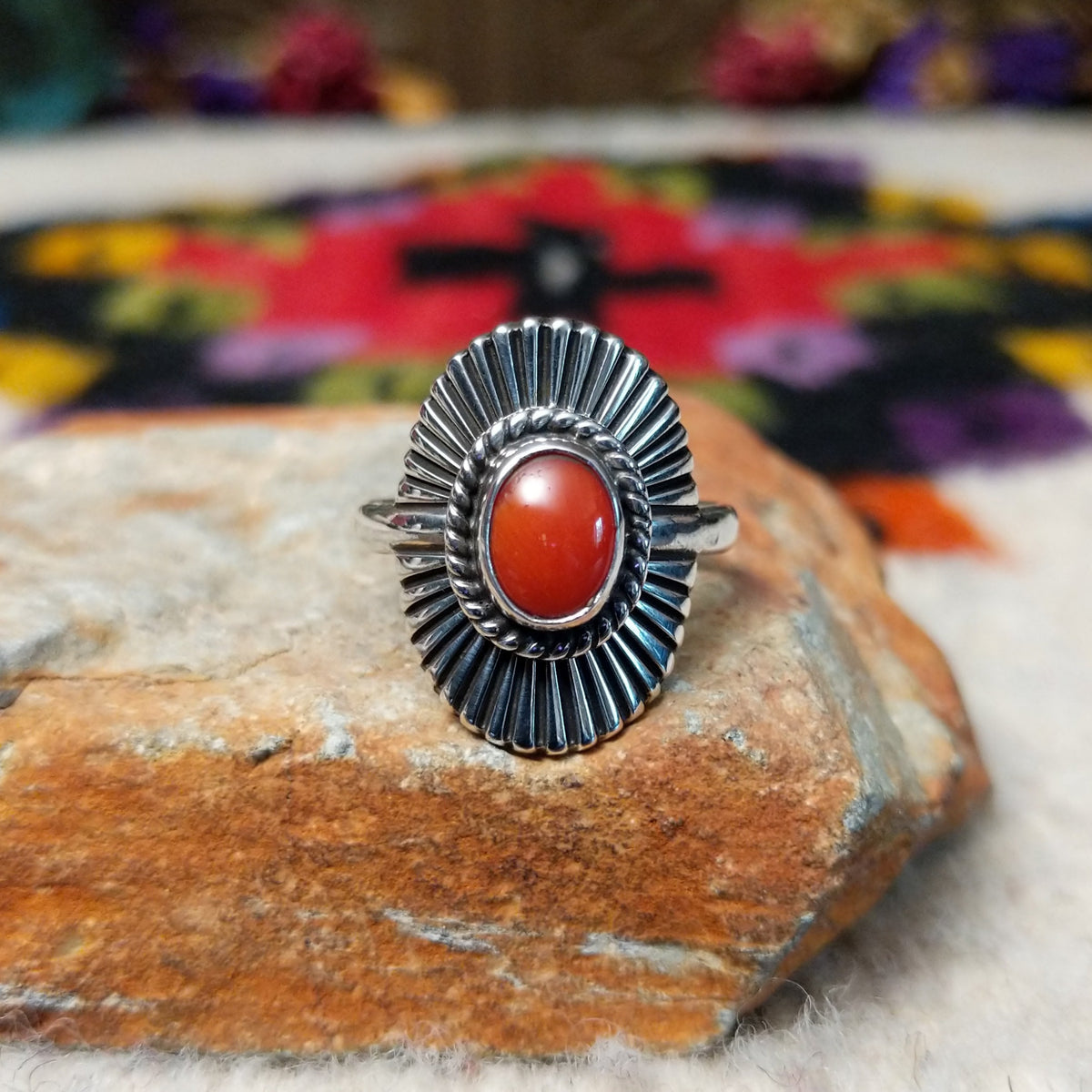 Striking Coral Ray Ring by Raymond Coriz featuring an oval red-orange coral stone framed by twisted sterling silver rope and radiating oxidized silver sunburst details.