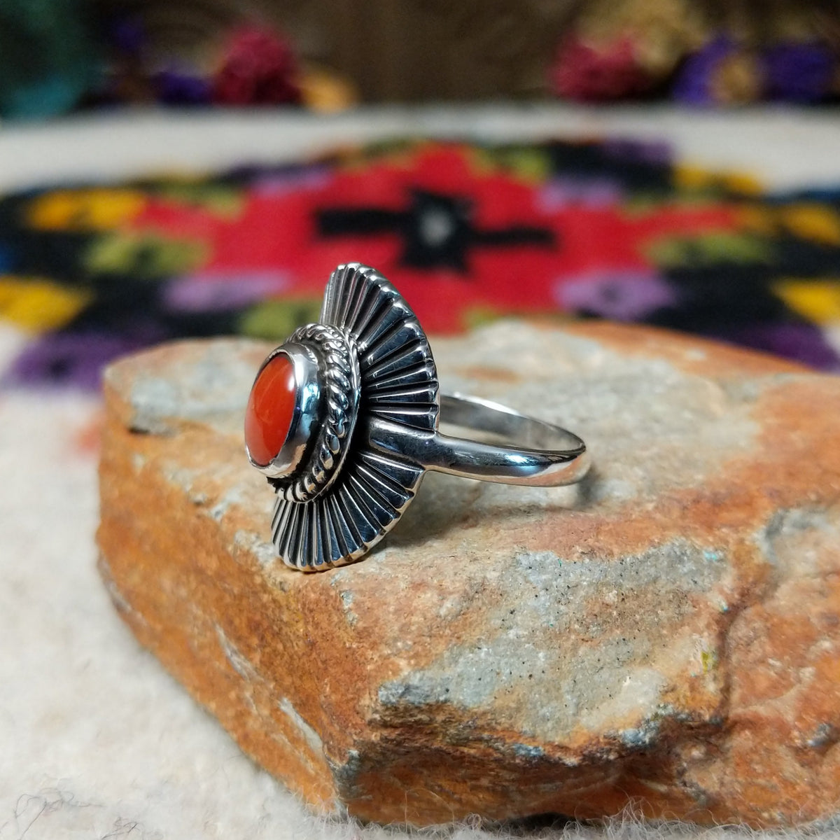 Striking Coral Ray Ring by Raymond Coriz featuring an oval red-orange coral stone framed by twisted sterling silver rope and radiating oxidized silver sunburst details; side view.