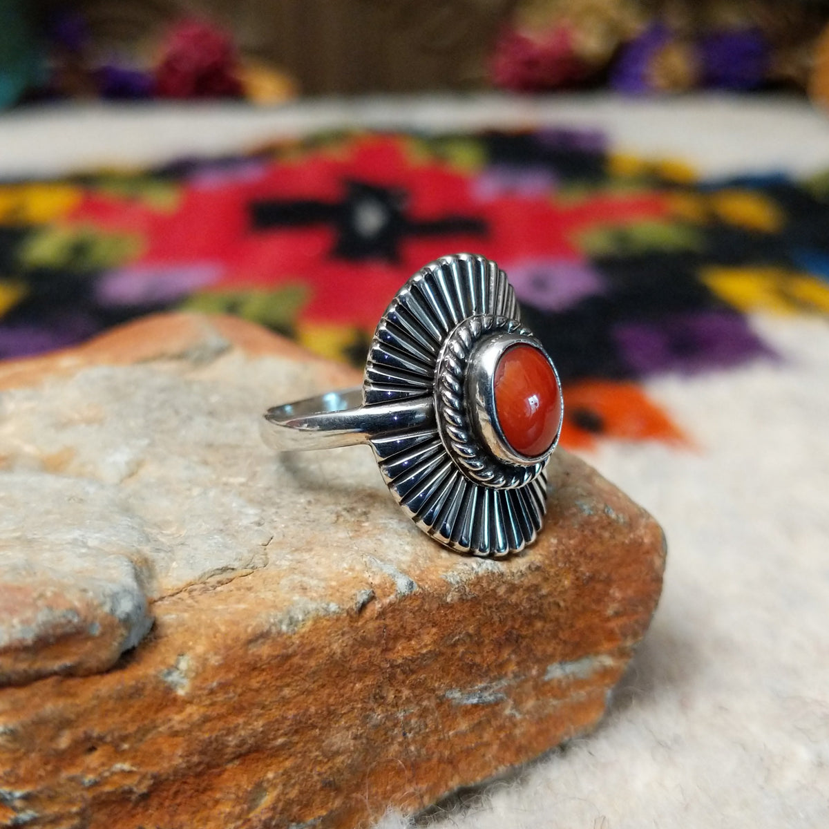Striking Coral Ray Ring by Raymond Coriz featuring an oval red-orange coral stone framed by twisted sterling silver rope and radiating oxidized silver sunburst details; side view.