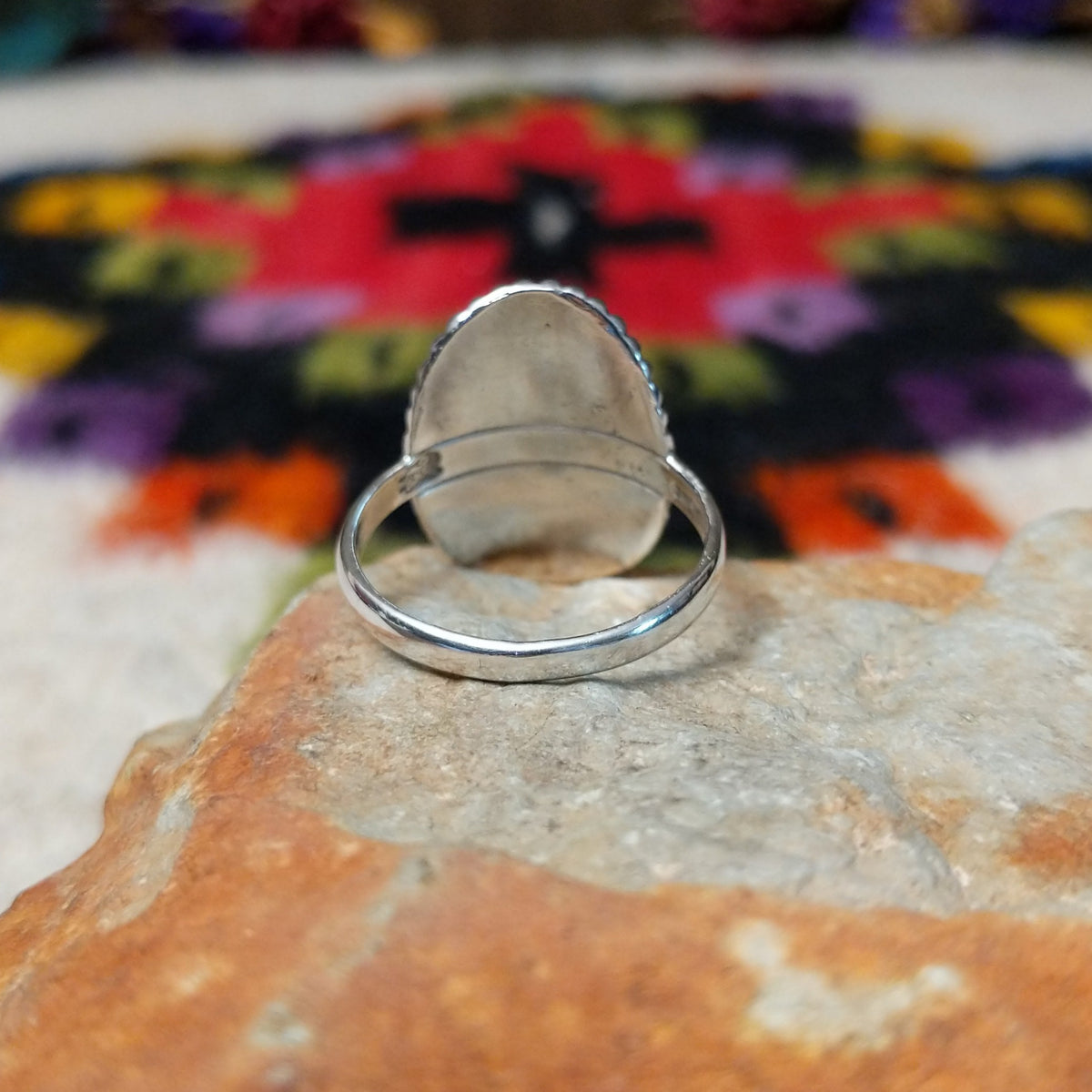 Striking Coral Ray Ring by Raymond Coriz featuring an oval red-orange coral stone framed by twisted sterling silver rope and radiating oxidized silver sunburst details; underside view.