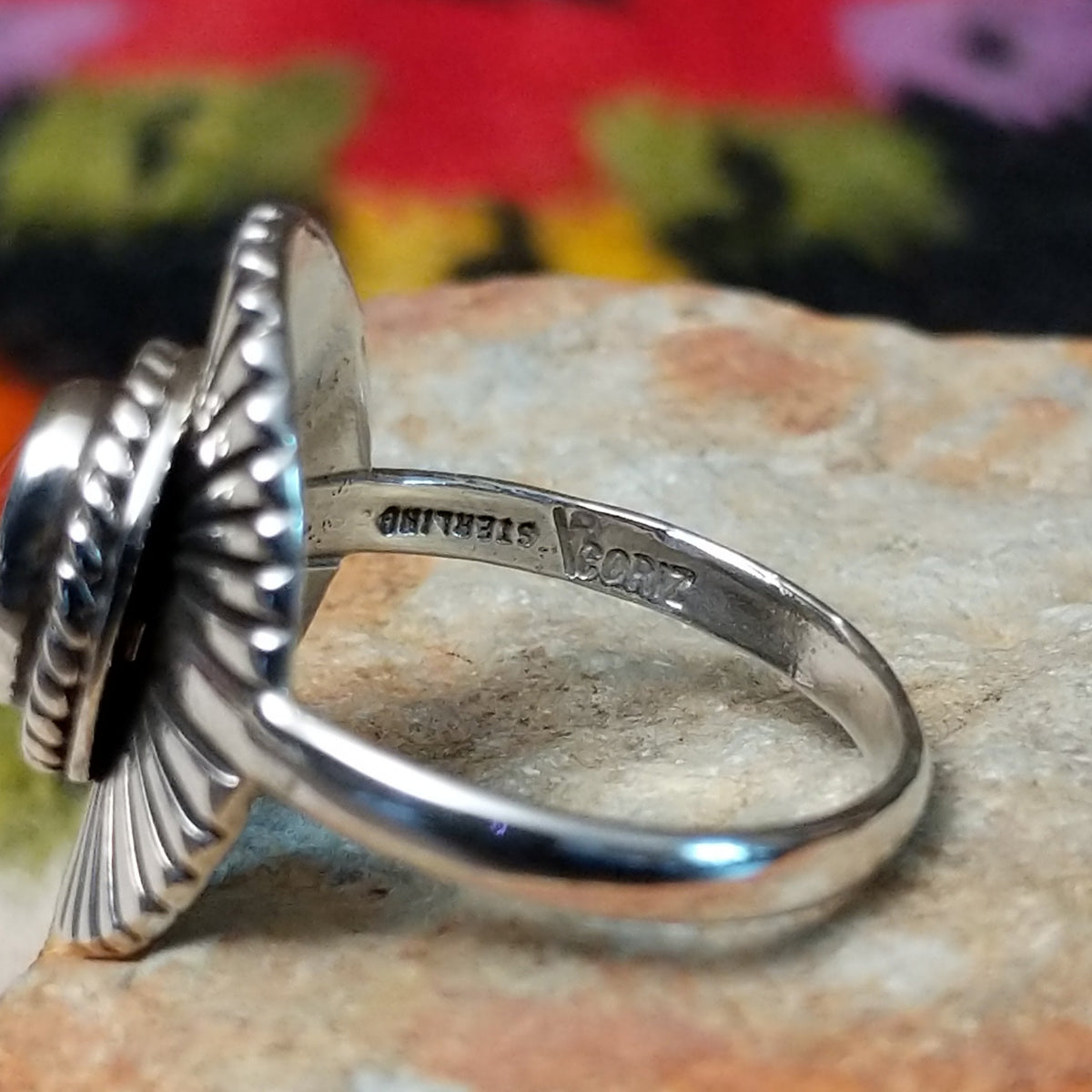 Striking Coral Ray Ring by Raymond Coriz featuring an oval red-orange coral stone framed by twisted sterling silver rope and radiating oxidized silver sunburst details; artisan and Sterling Silver stamp.