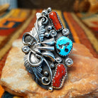 Coral & Turquoise Feather Ring by Jason Livingston featuring an oval turquoise stone, two elongated coral stones, intricate silver feather detailing, decorative scrollwork, polished silver beads, and stamped accents in an elaborate Southwestern design.