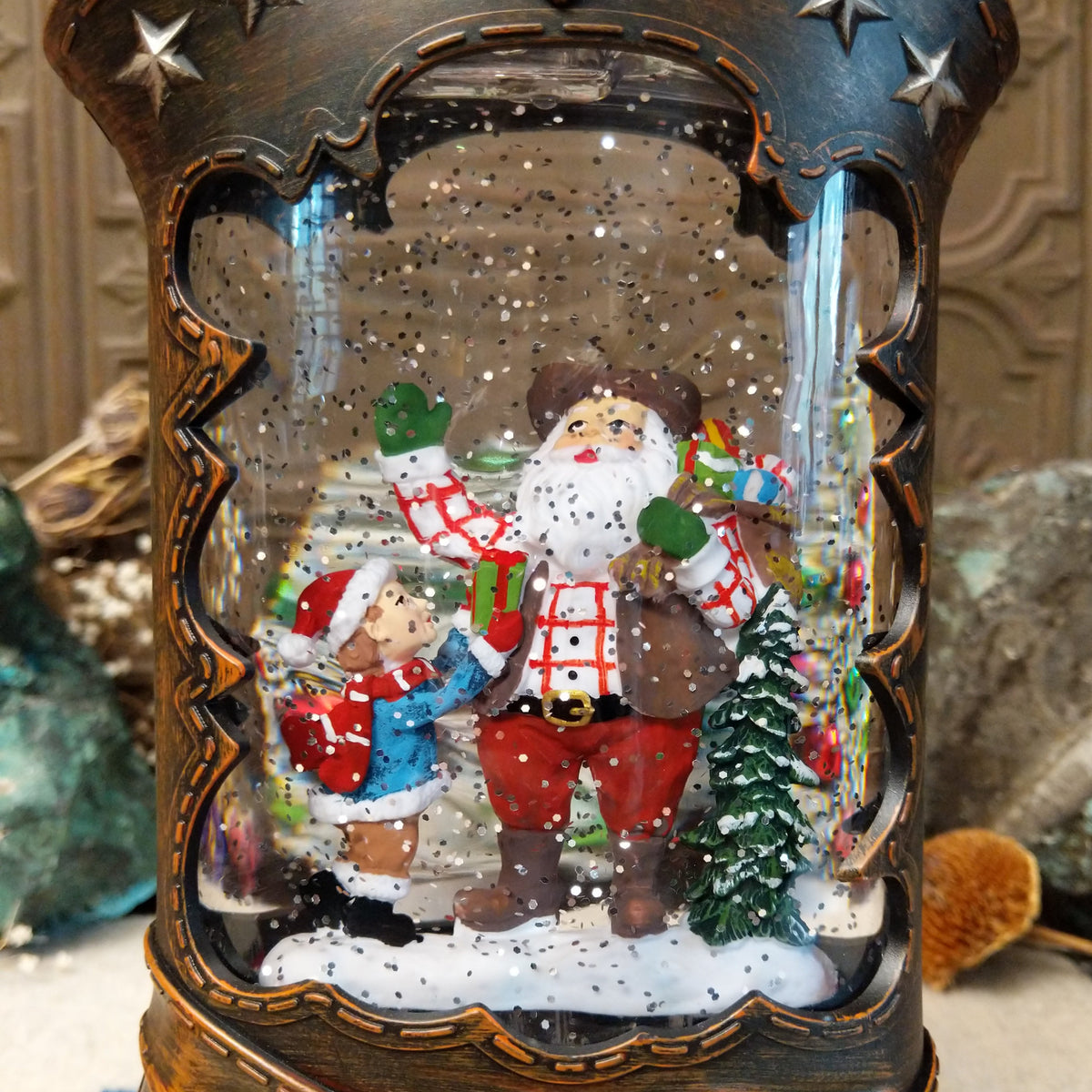 Cowboy Boot Santa Snow Globe featuring cowboy-style Santa with a child, presents, and a snowy evergreen inside a rustic brown Western boot decorated with silver stars and studs.