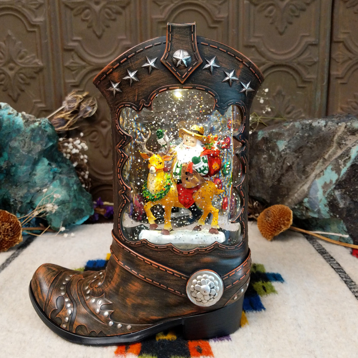 Cowboy Boot Santa Riding Reindeer Snow Globe featuring Western-style Santa riding a decorated reindeer inside a rustic brown cowboy boot with silver stars and sparkling snow.