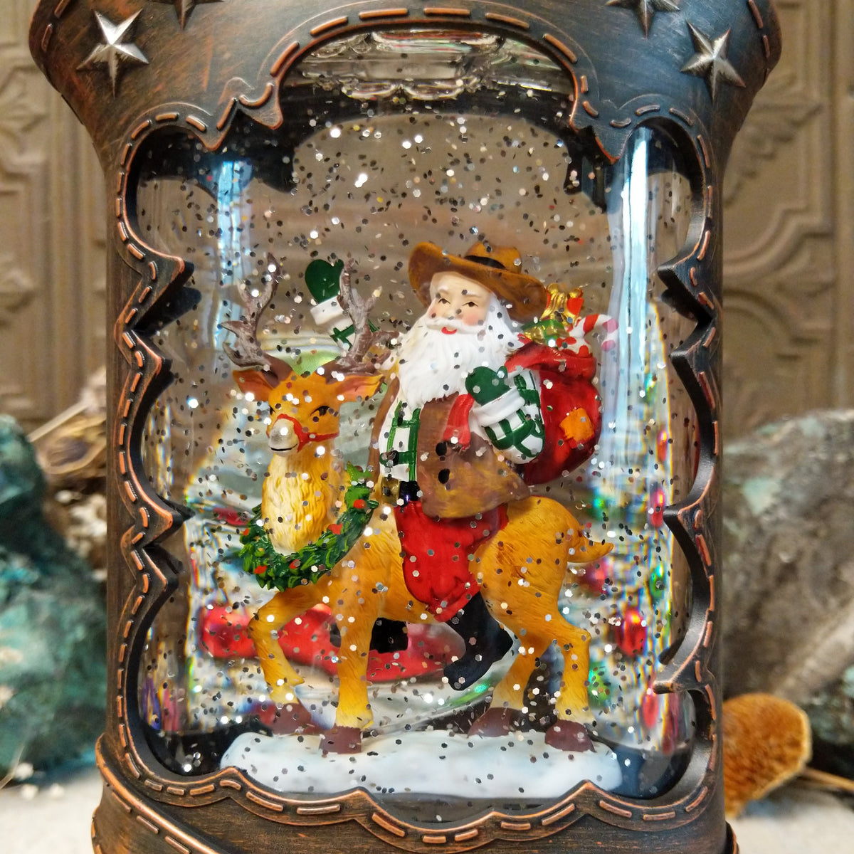 Cowboy Boot Santa Riding Reindeer Snow Globe featuring Western-style Santa riding a decorated reindeer inside a rustic brown cowboy boot with silver stars and sparkling snow.