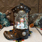 Cowboy Boot Snowmen Snow Globe featuring two snowmen and a snowy evergreen tree inside a rustic brown Western boot decorated with silver stars and studs.