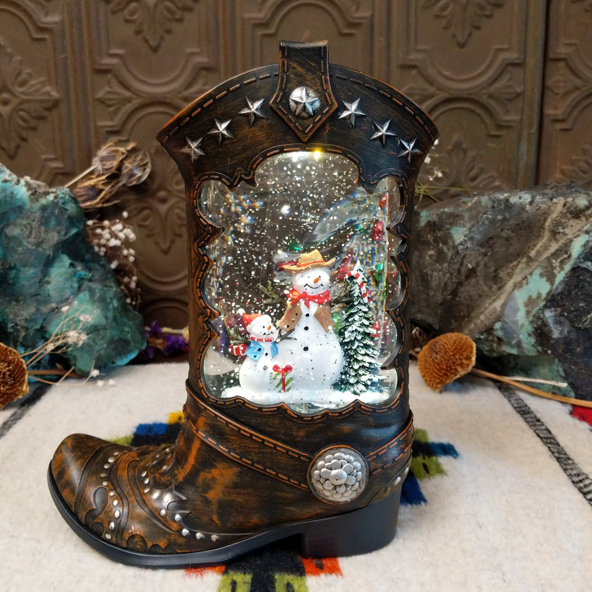 Cowboy Boot Snowmen Snow Globe featuring two snowmen and a snowy evergreen tree inside a rustic brown Western boot decorated with silver stars and studs.