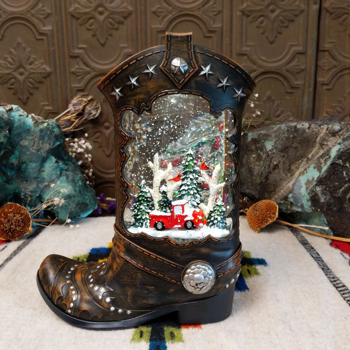 Festive Cowboy Boot Truck Snow Globe featuring a red vintage pickup truck surrounded by snow-covered trees inside a dark brown Western boot with silver stars and concho detailing.