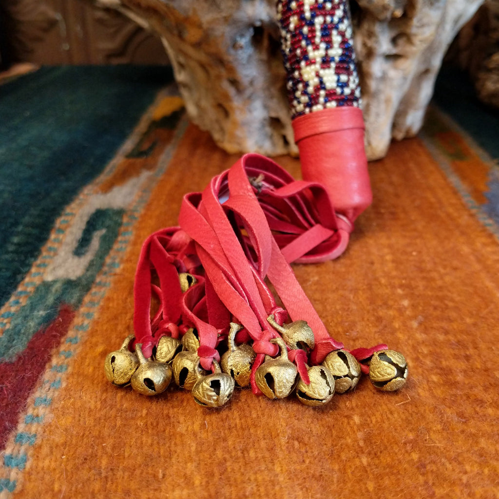 The bottom of the shaft features brass bells tethered to the leather fringe.