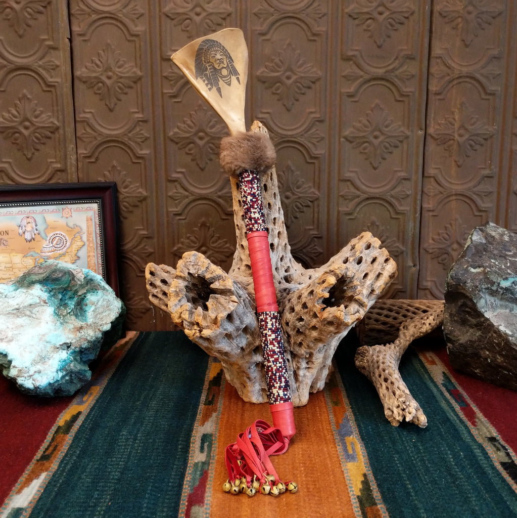 Deer shoulder blade engraved with headdress design on the top of the shaft that is decorated with colorful beading and red leather.