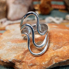 Handcrafted sterling silver ring by Raymond Coriz featuring a polished openwork design with flowing curved silver forms and a contemporary sculptural style.