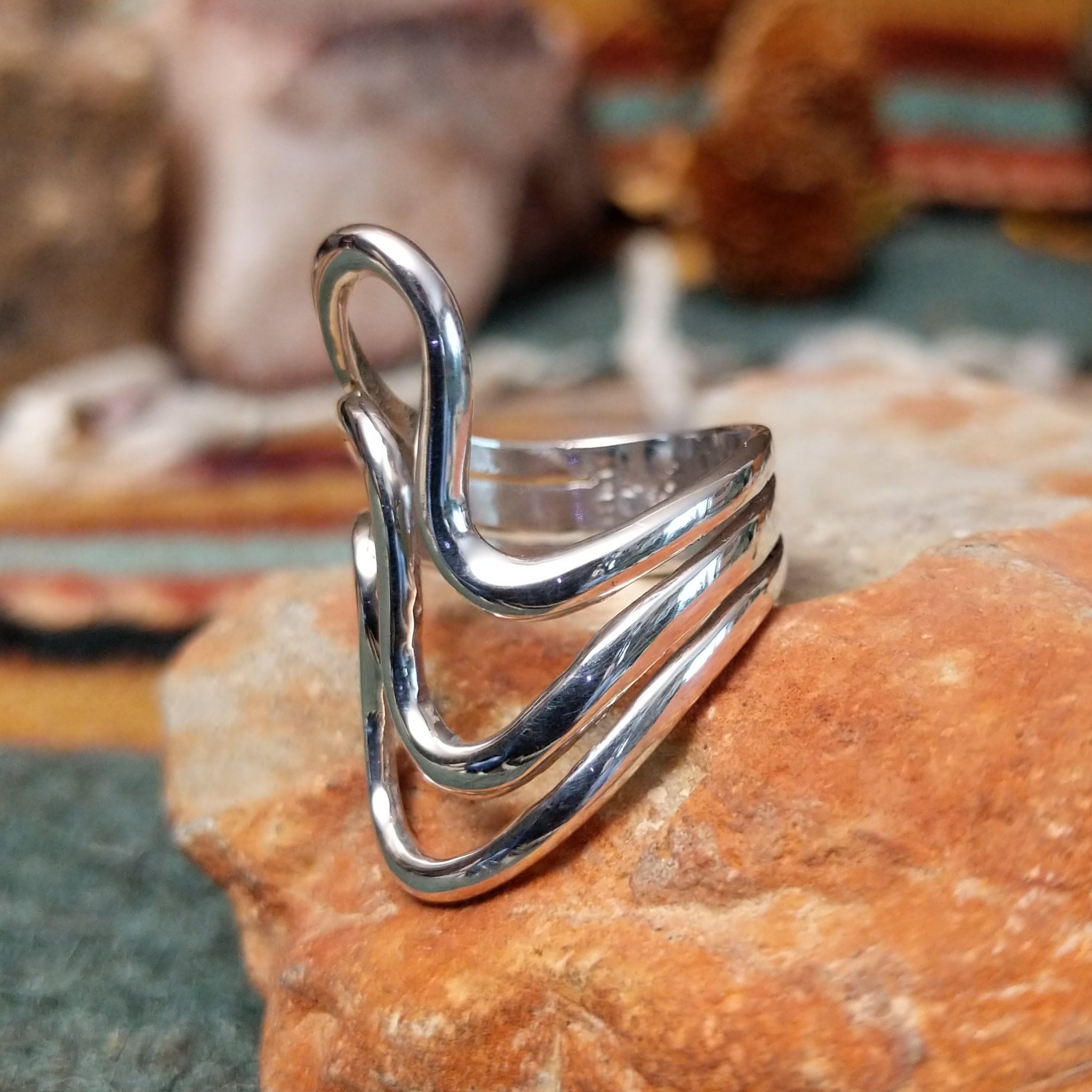 Handcrafted sterling silver ring by Raymond Coriz featuring a polished openwork design with flowing curved silver forms and a contemporary sculptural style; side view.