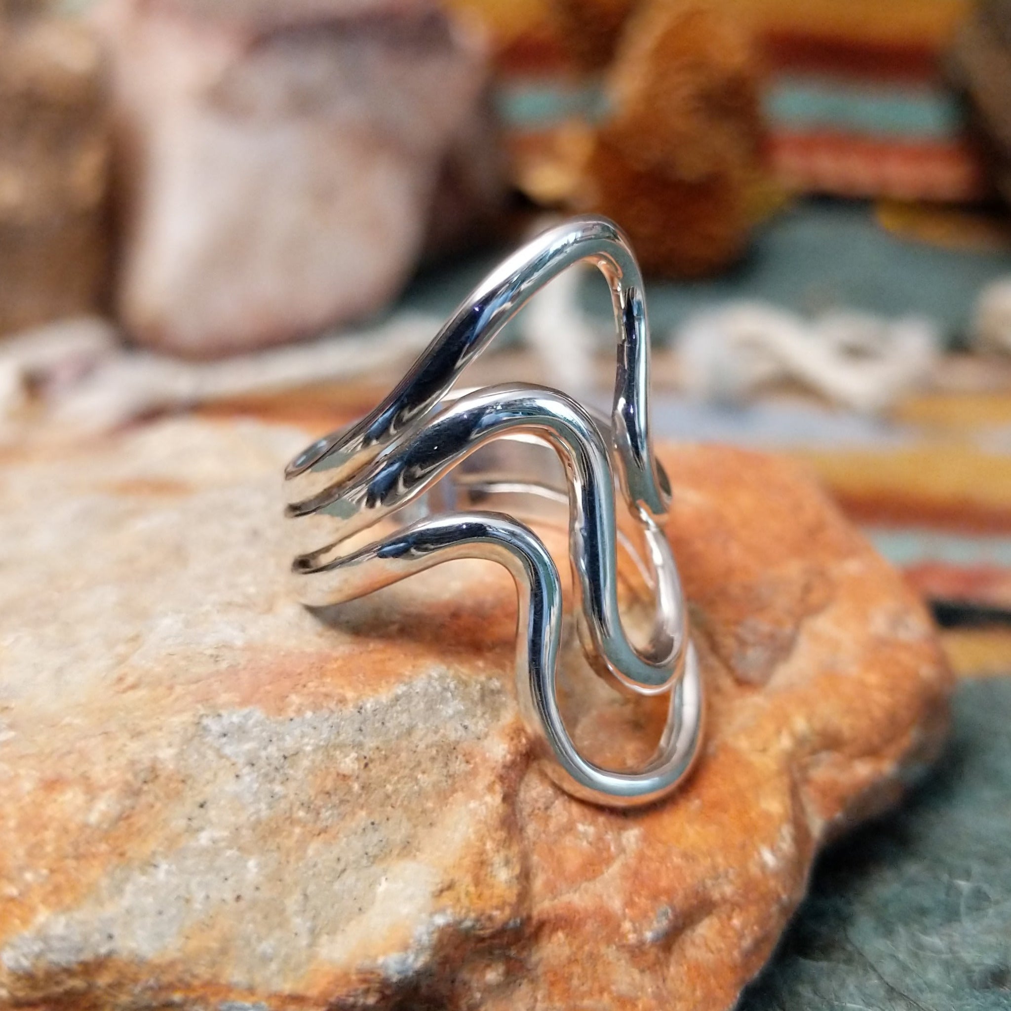 Handcrafted sterling silver ring by Raymond Coriz featuring a polished openwork design with flowing curved silver forms and a contemporary sculptural style; side view.