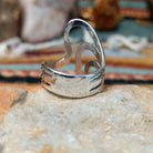 Handcrafted sterling silver ring by Raymond Coriz featuring a polished openwork design with flowing curved silver forms and a contemporary sculptural style; underside view.