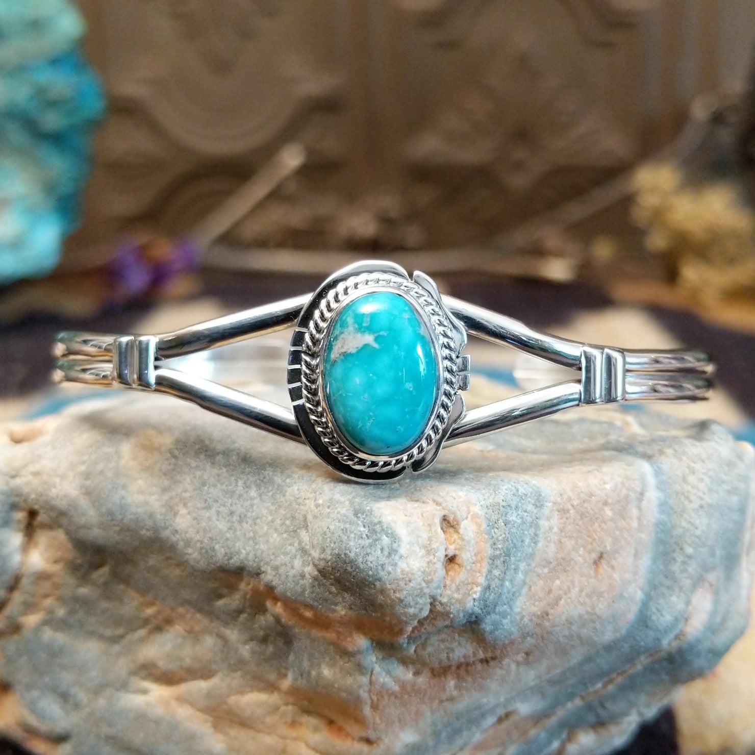 Sterling silver bracelet with turquoise set in an oval bezel, framed by twisted rope and an incised setting.
