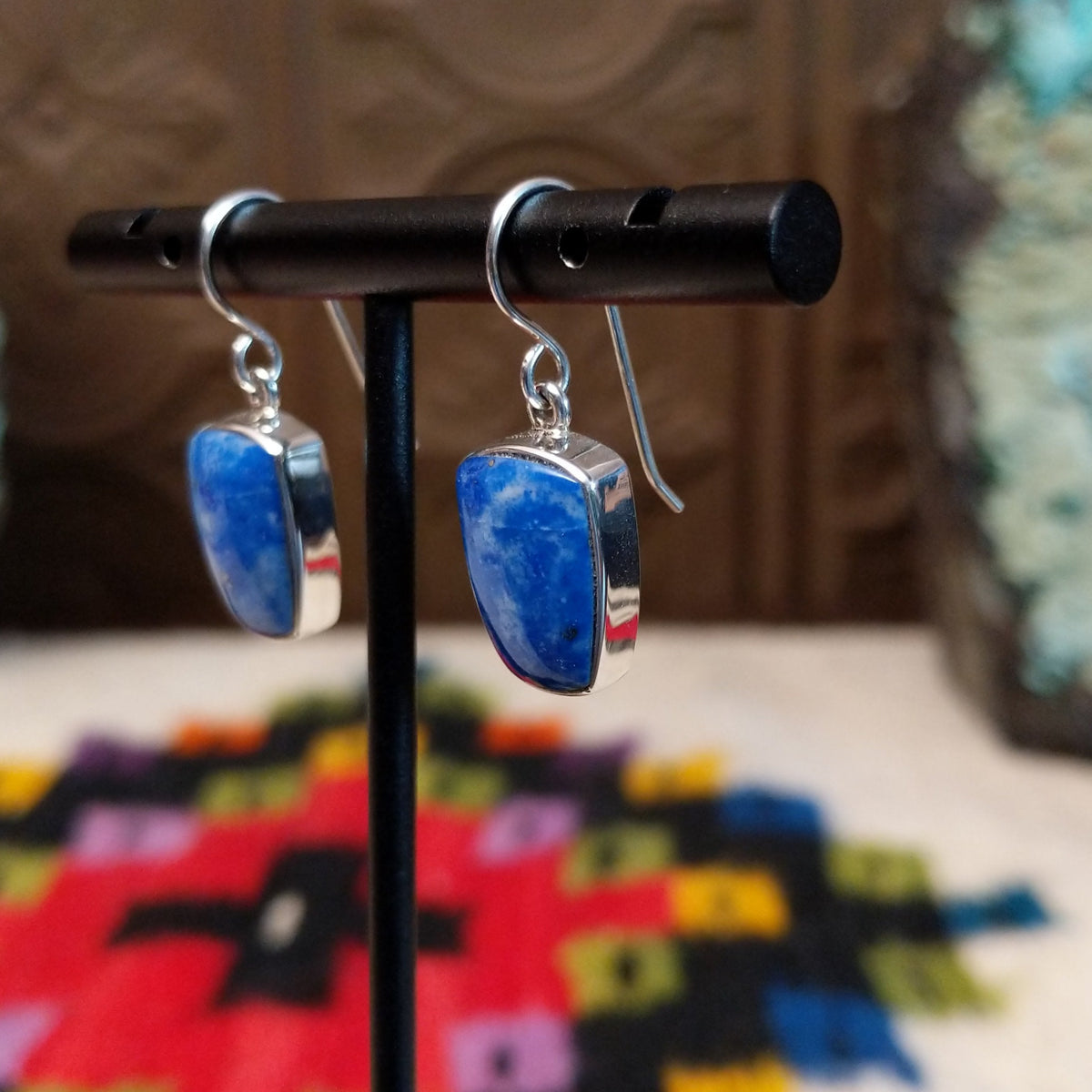 Denim Lapis Earrings by Cathy Webster featuring polished blue stones with cloudy light-blue and white variations, set in smooth silver bezels and suspended from French ear wires; side view.