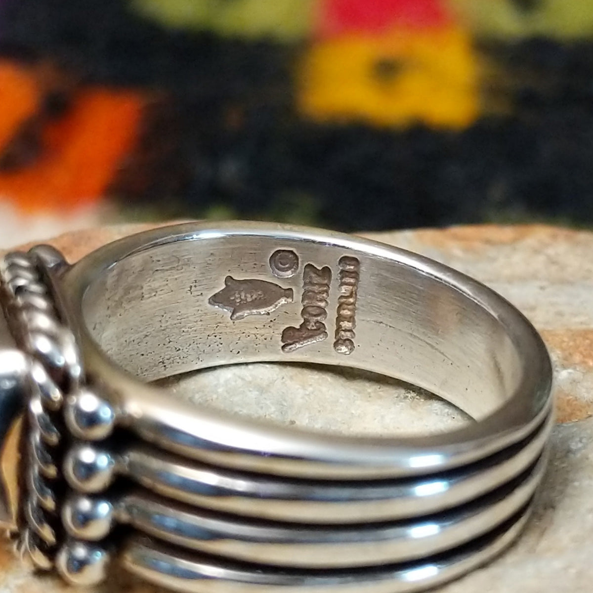 Denim lapis ring by Raymond Coriz with square stone, twisted silver border, and four-row band. Close up of the artist's stamped signature.