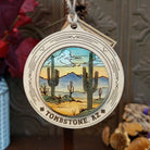 Desert Saguaro Sunrise Wood Ornament featuring tall green cacti, distant blue mountains, colorful sunrise sky, engraved circular wooden frame, “Tombstone, AZ” lettering, and natural twine hanging loop.