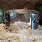 Wide sterling silver cuff bracelet with raised geometric silverwork, hand-stamped details, and oxidized accents.