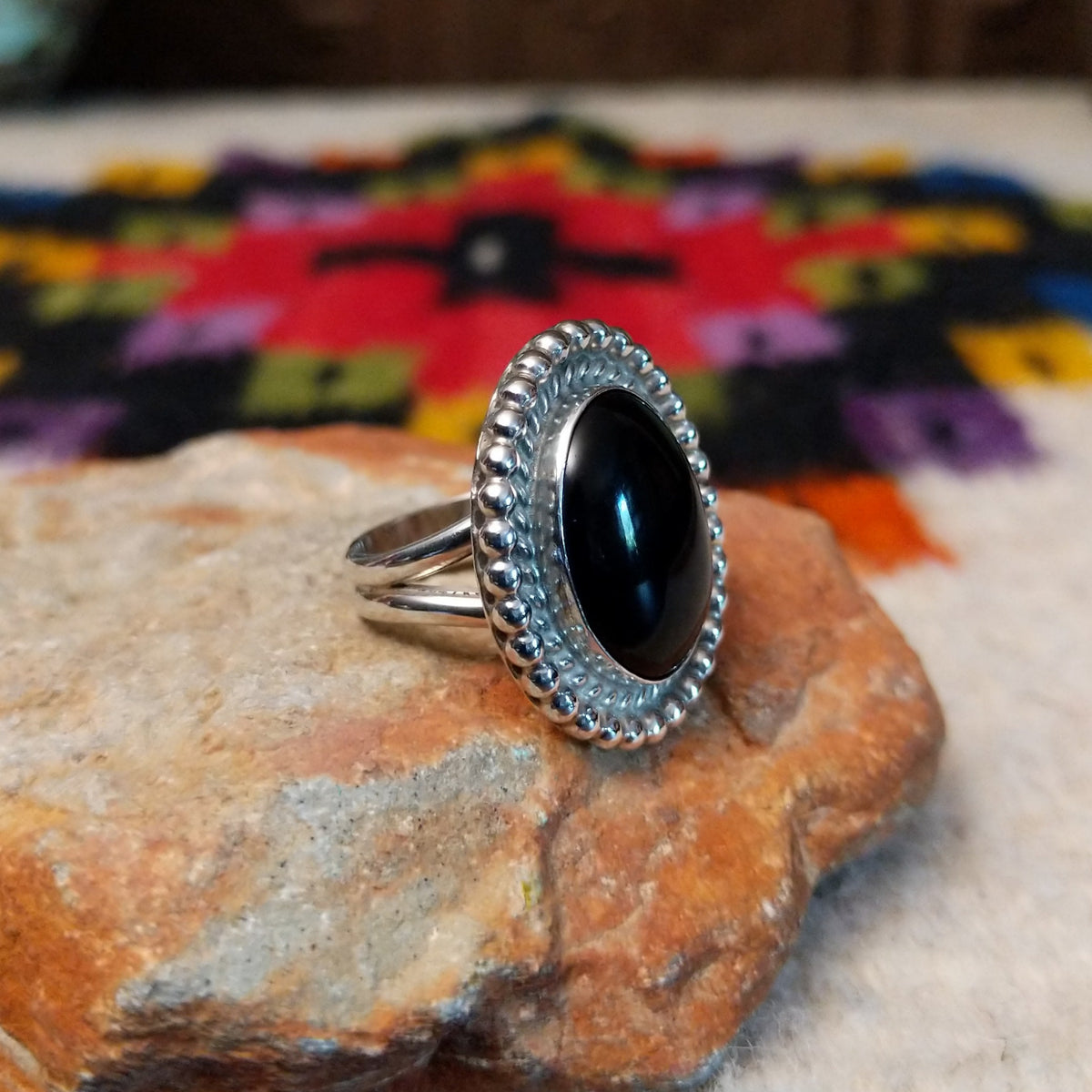 This Black Onyx Ring by J. Frank features a large oval black onyx stone set in sterling silver with twisted rope detailing and a raised beaded border; side view.