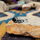 Handcrafted sterling silver Navajo ring featuring a polished oval Black Onyx cabochon in a smooth bezel setting, accented by decorative sterling silver bead clusters on each side of the gemstone; side view.