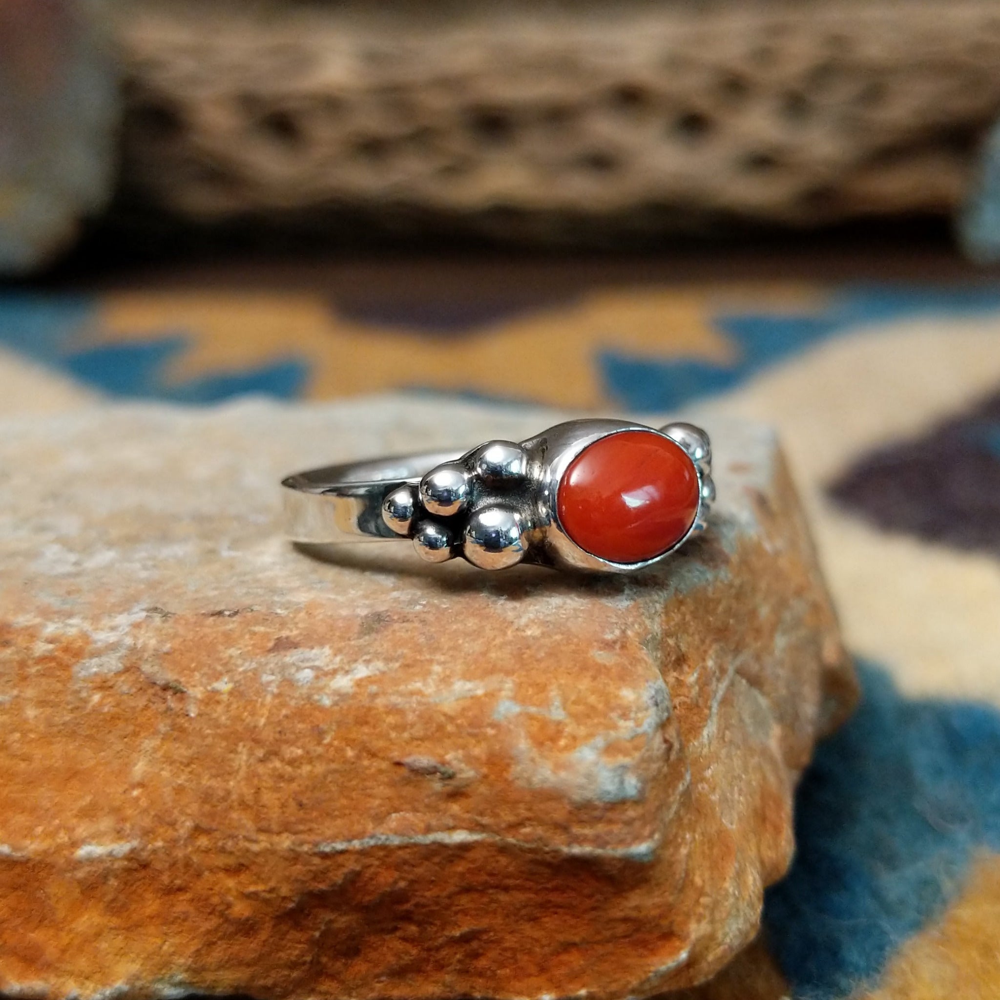 Handcrafted sterling silver dotted coral ring by Lowell Draper, featuring an oval coral cabochon with polished silver bead accents; side view.