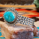 Sterling silver cuff with Kingman turquoise set in a large, oval bezel that is framed by dotted accents, while the band features a unique twist design.