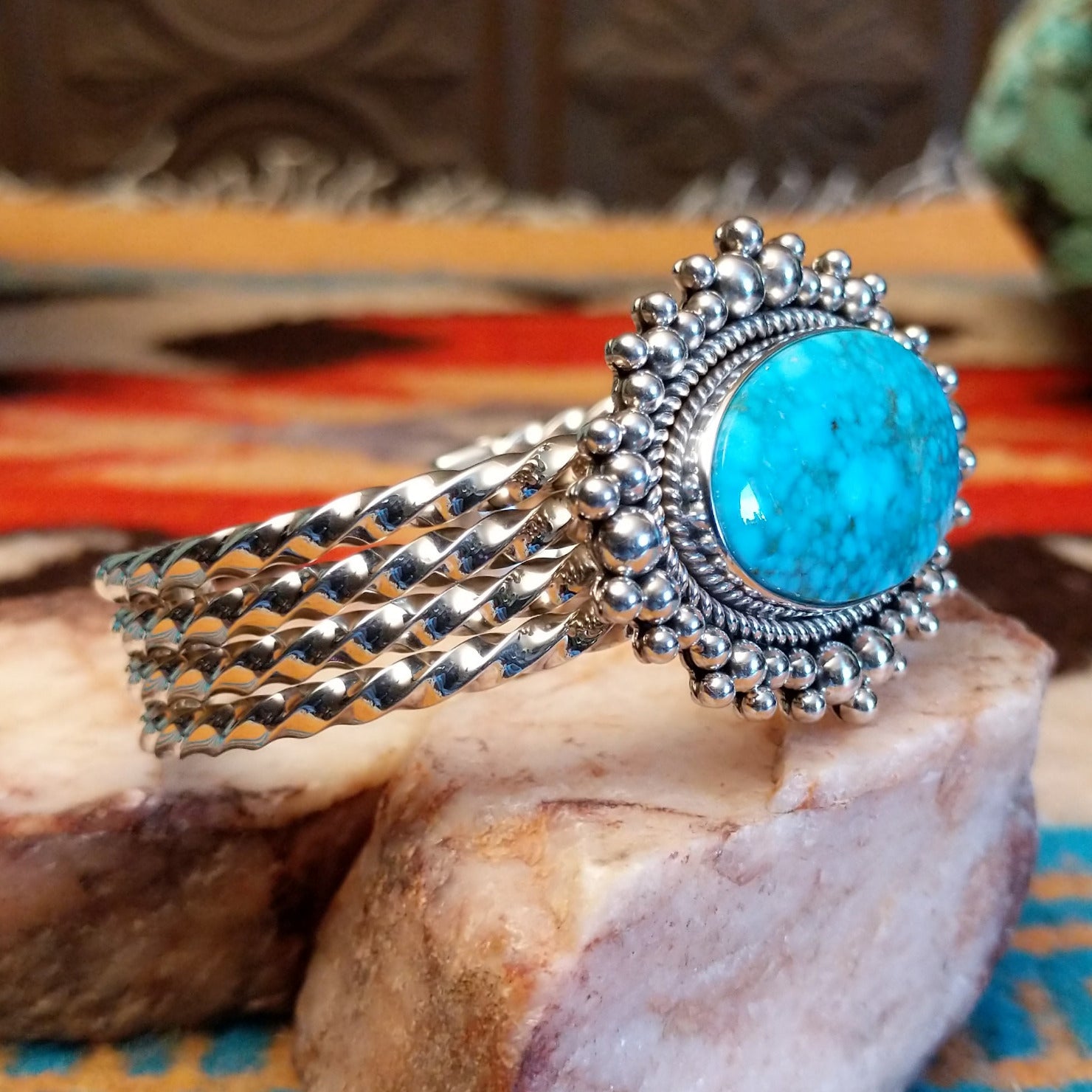 Sterling silver cuff with Kingman turquoise set in a large, oval bezel that is framed by dotted accents, while the band features a unique twist design.
