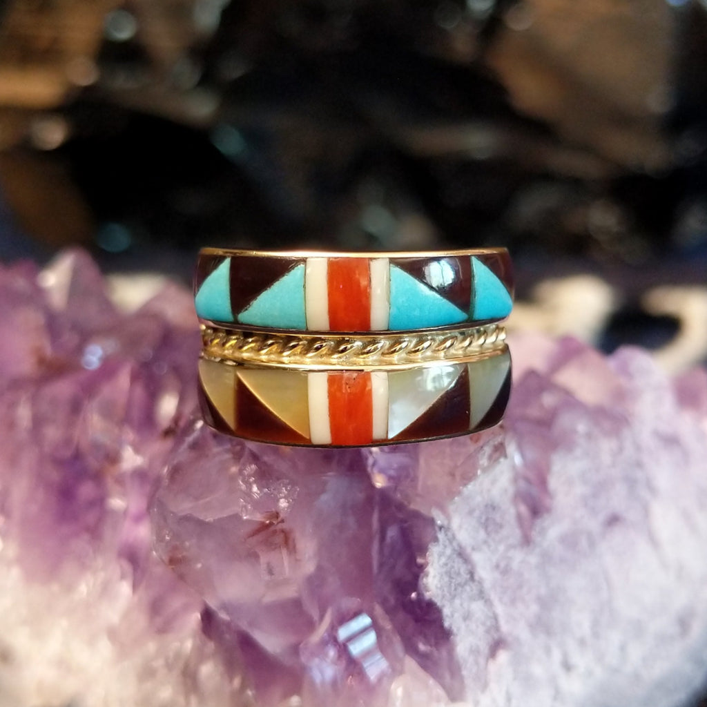A gold ring with two stacked rows of geometric inlays divided by a twisted gold rope.