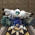 Navajo-made eagle kachina doll by M. C. with outstretched feathered wings, blue mask, yellow beak, and white feather collar.