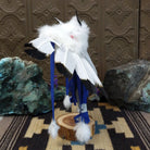 Navajo-made eagle kachina doll by M. C. with outstretched feathered wings, blue mask, yellow beak, and white feather collar.