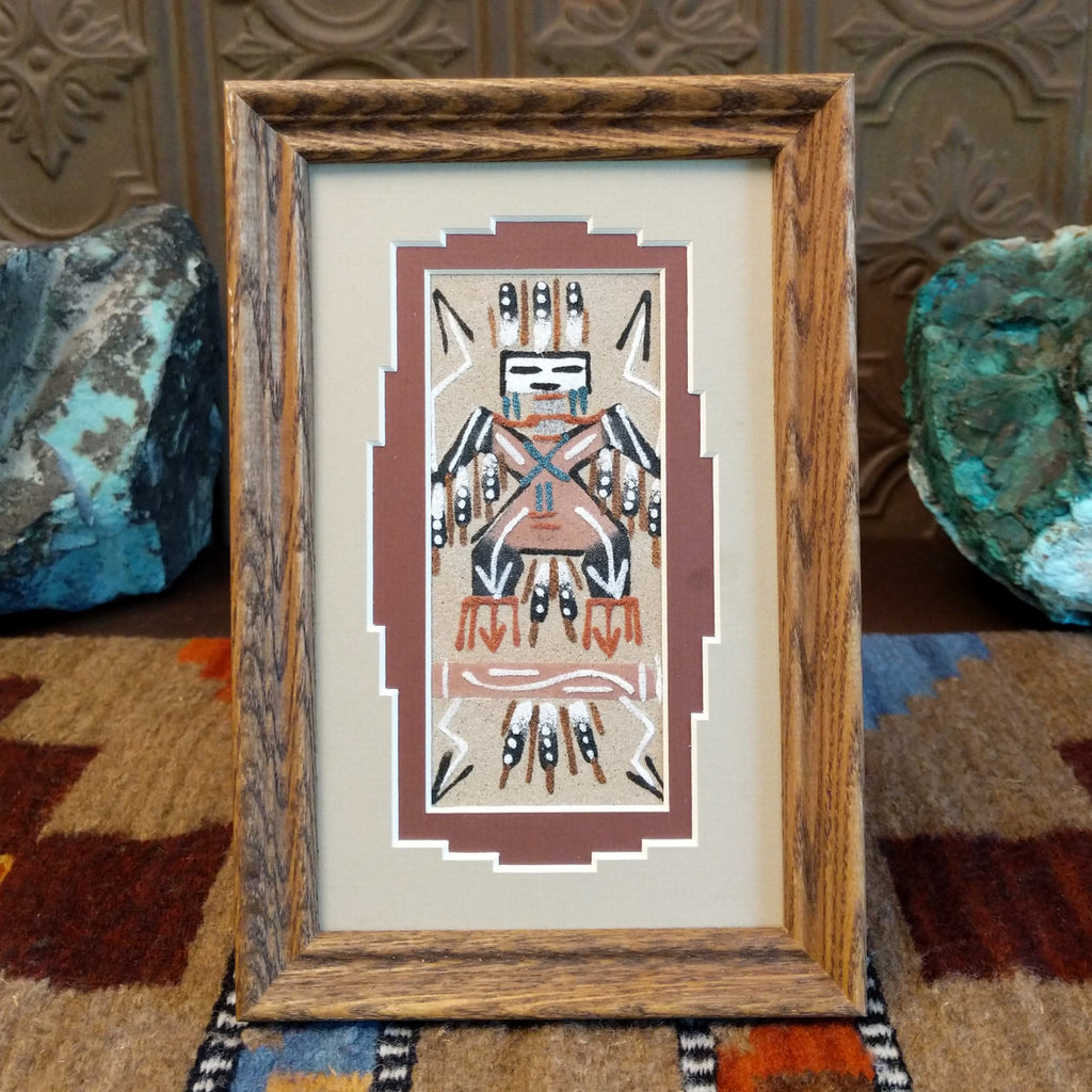 Multicolored sand painting of an Eagle Dancer set within a wooden frame.