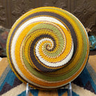 Handwoven earth tone wire art bowl by Bridge for Africa featuring a spiral pattern in recycled wire with golden yellow, olive green, ivory, brown, and tan tones, perfect for home décor or wall display; underside view.