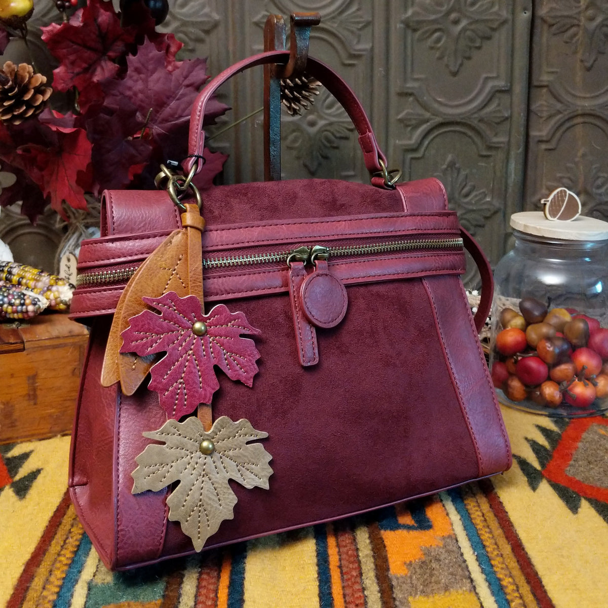 Emma Crossbody Bag by Liz Soto featuring a structured silhouette, mixed-texture panels, top handle, zippered compartment, decorative zipper pulls, and layered leaf-shaped charms.