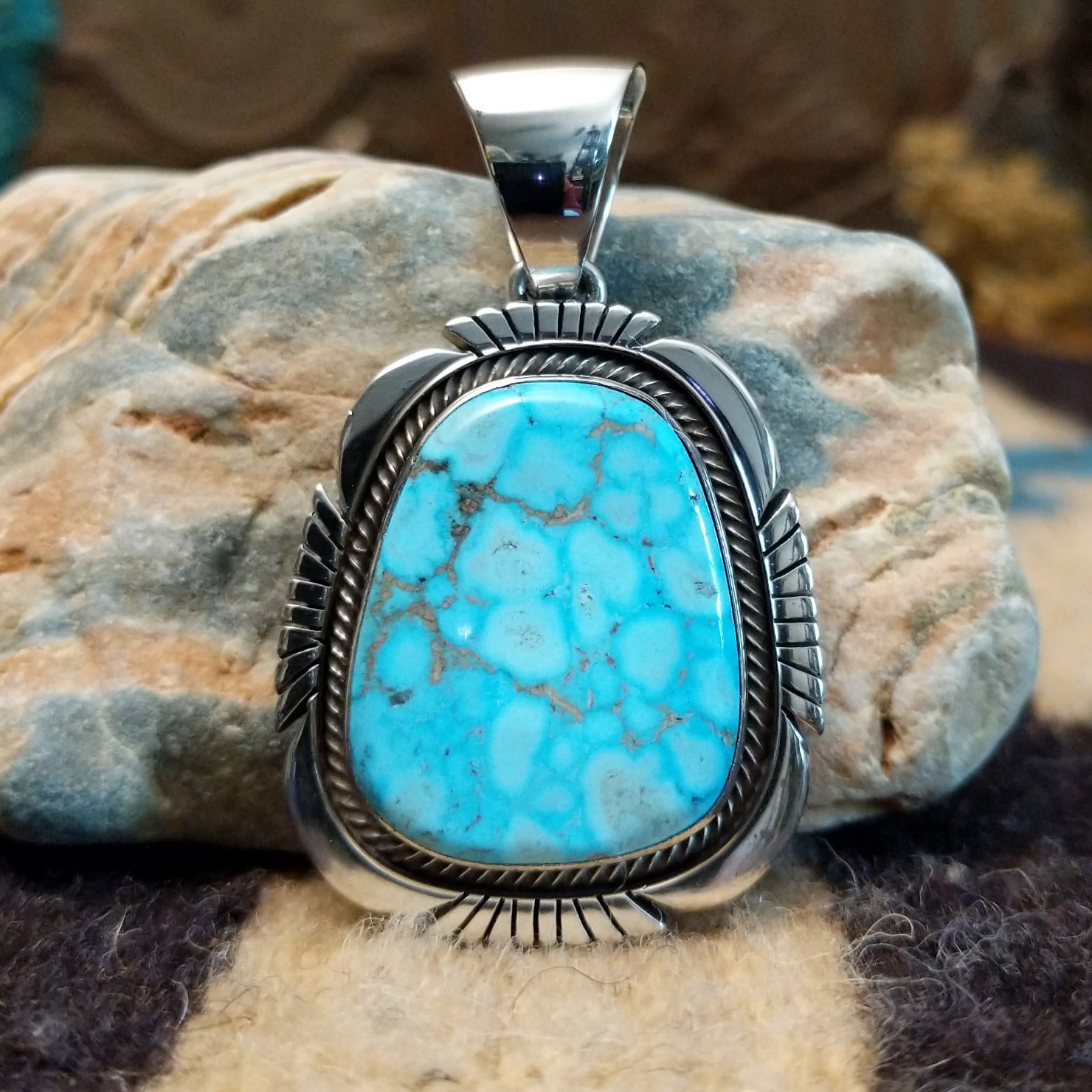 Sterling silver pendant with turquoise set in a large bezel, framed by twisted rope and etched designs.