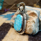 Sterling silver pendant with turquoise set in a large bezel, framed by twisted rope and etched designs.
