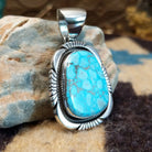 Sterling silver pendant with turquoise set in a large bezel, framed by twisted rope and etched designs.