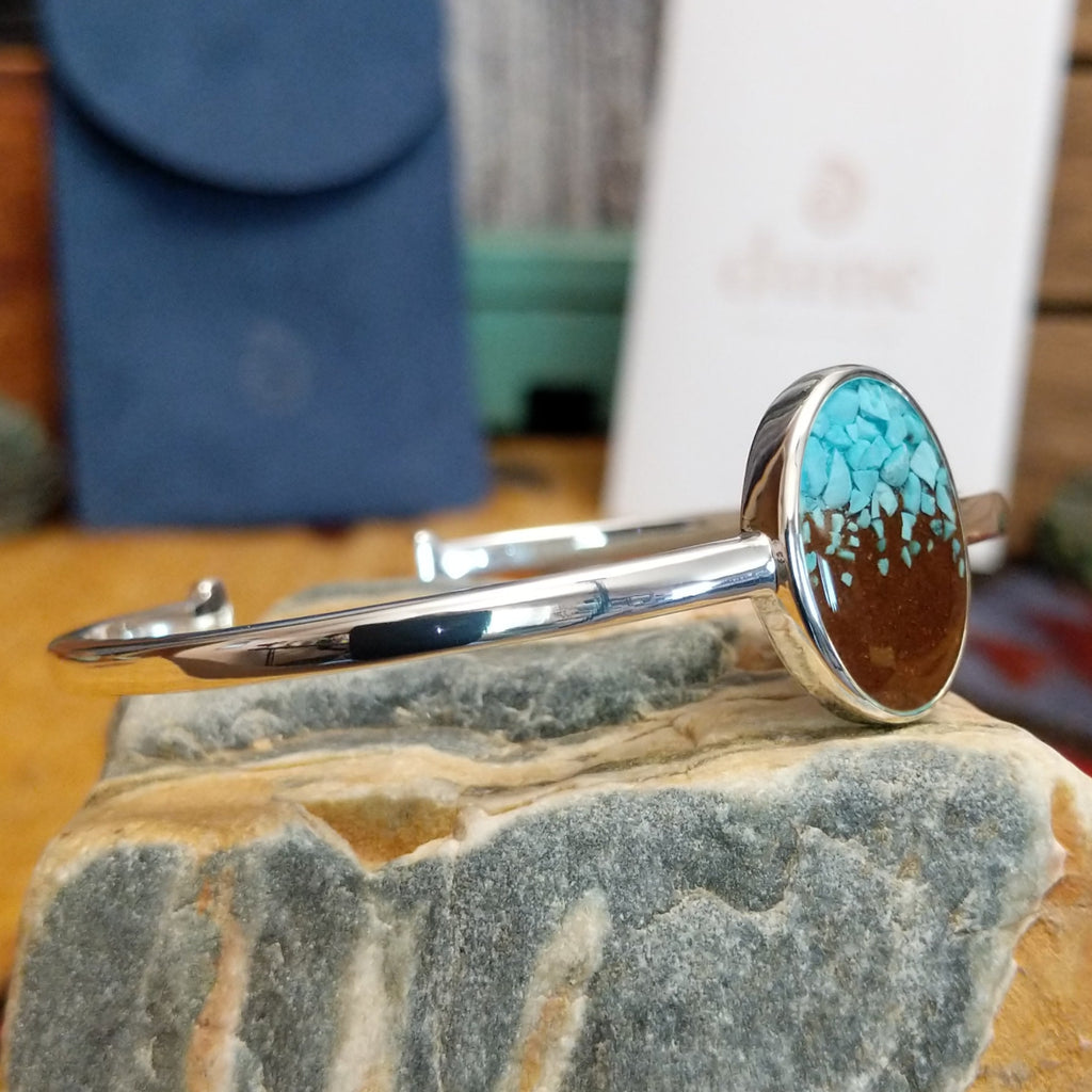 Oval cuff with a silver-plated brass frame, featuring turquoise and brown sand.