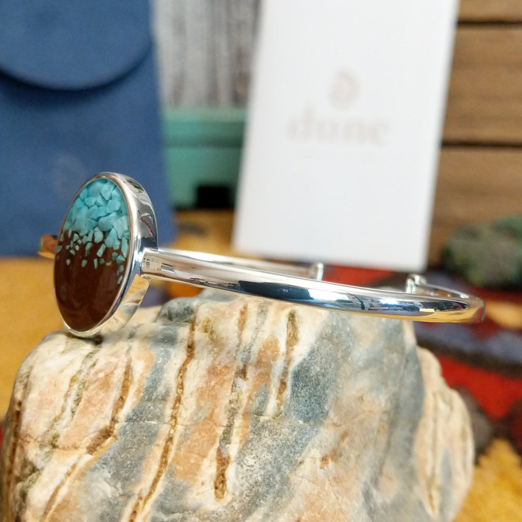 Oval cuff with a silver-plated brass frame, featuring turquoise and brown sand.