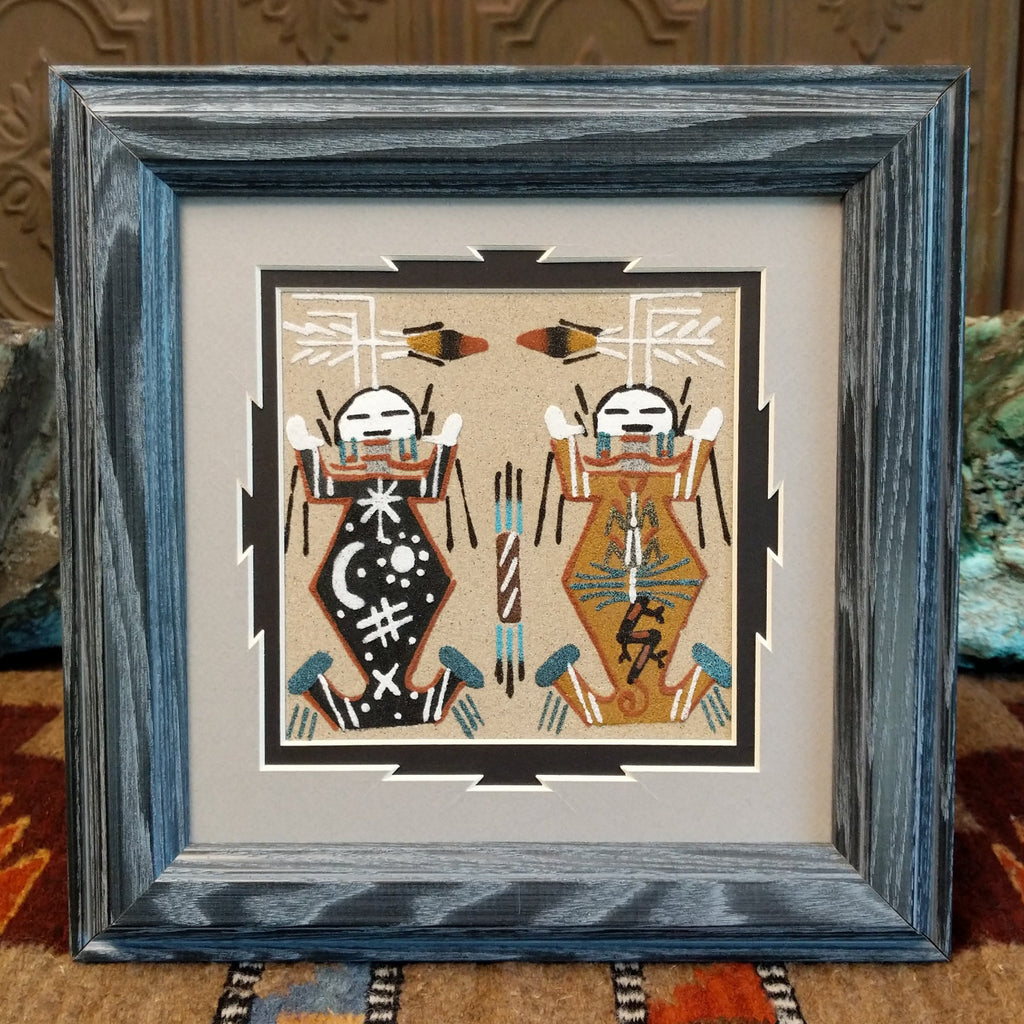 Father Sky and Mother Earth depicted using colorful sand and set within a painted blue wooden frame.