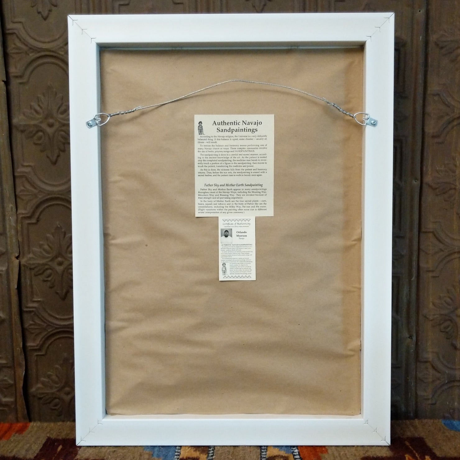 The back features a wire hook and artisan's information.
