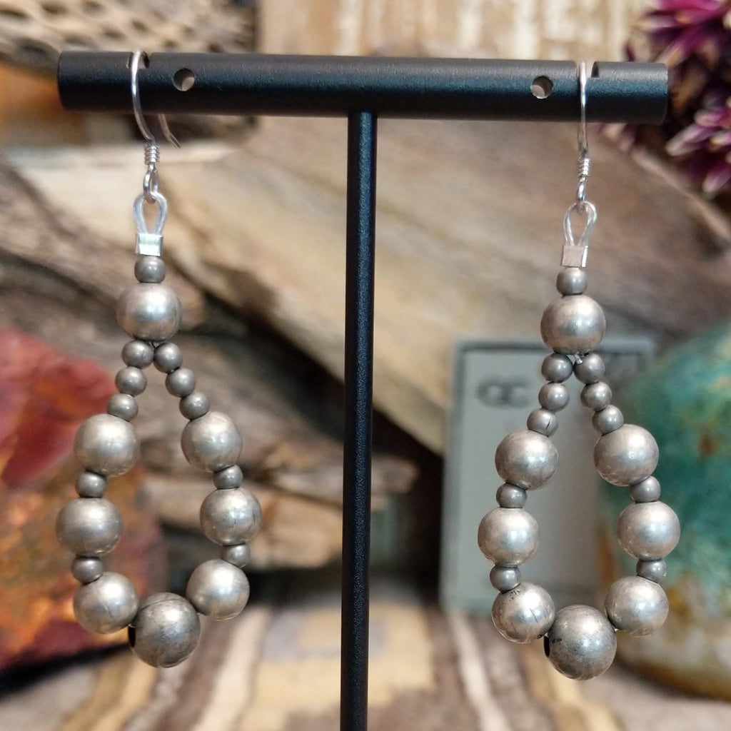A pair of silver earrings, featuring a cascade of polished spherical beads.