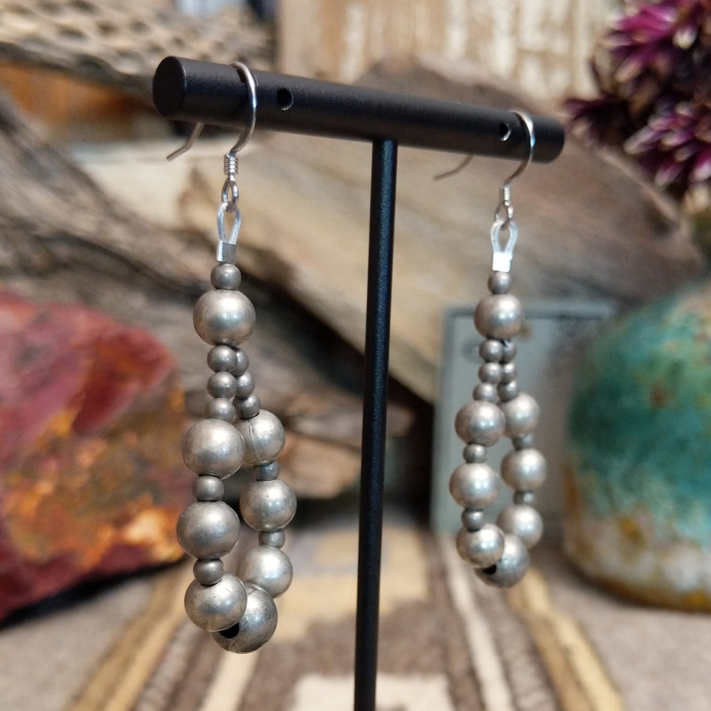 A pair of silver earrings, featuring a cascade of polished spherical beads.