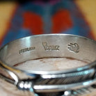 Feather loop ring by Raymond Coriz, featuring a detailed handcrafted feather design wrapped around a polished sterling silver band with traditional Southwestern-inspired craftsmanship.  Artisan and Sterling Silver stamp.