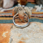 Handcrafted sterling silver ring by Allen Chee featuring an oval natural turquoise cabochon with dark matrix, surrounded by detailed feather motifs, silver scrollwork, twisted wire, and bead accents; underside view.