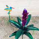 A large purple metal flower and a multicolor hummingbird.